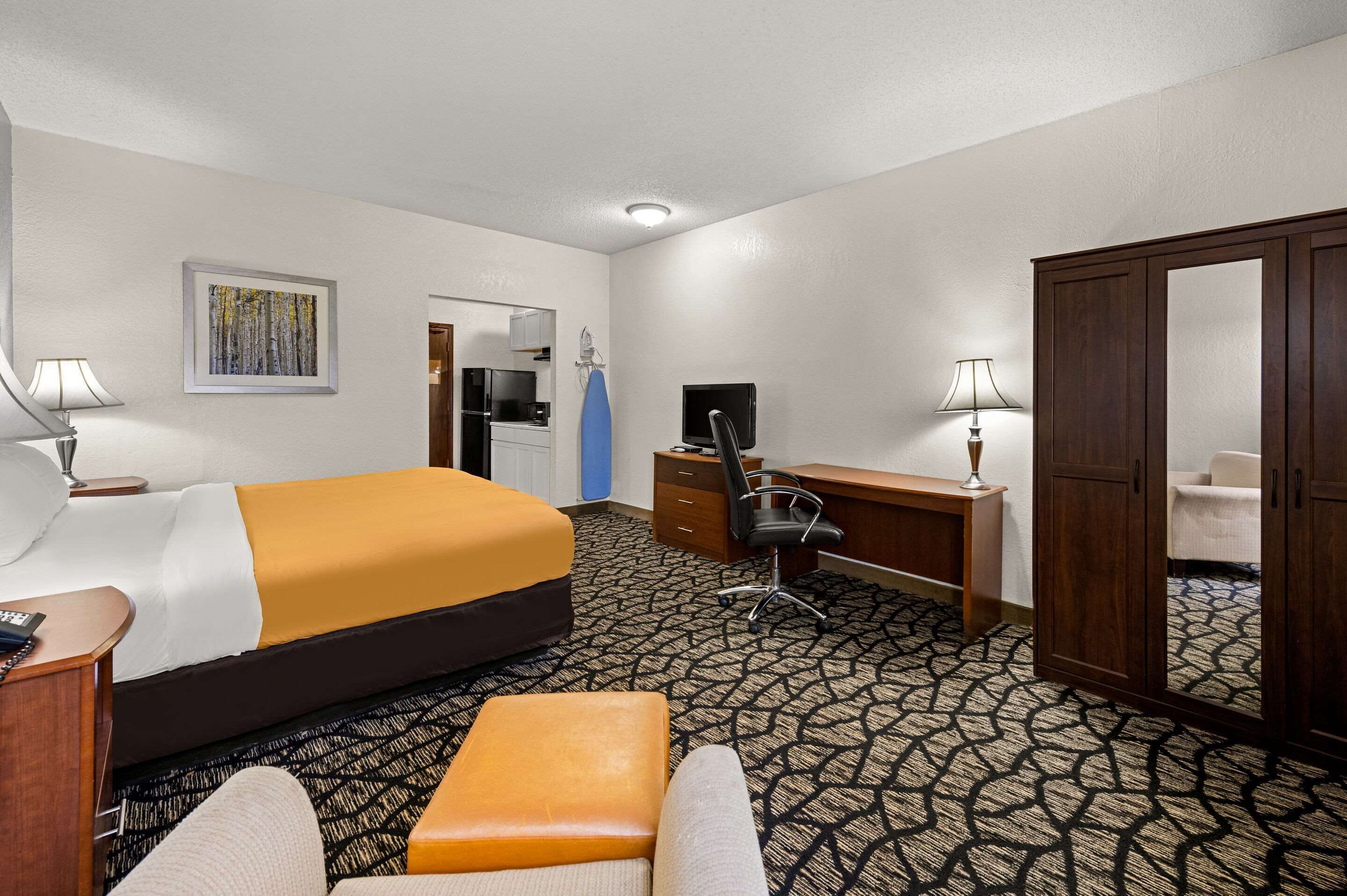 A hotel room with a large bed, a desk, a chair, a wardrobe, and a bathroom visible through an open door.