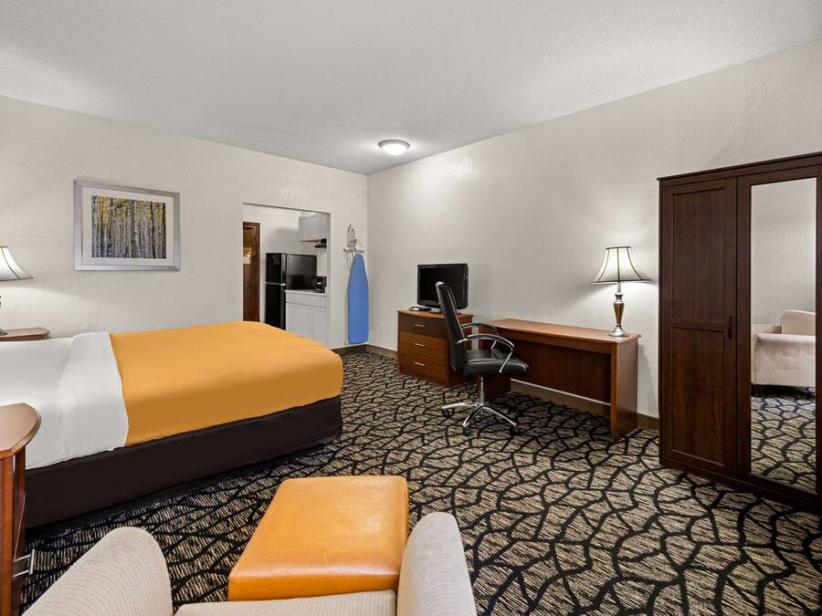 A hotel room with a large bed, a desk, a chair, a wardrobe, and a bathroom visible through an open door.