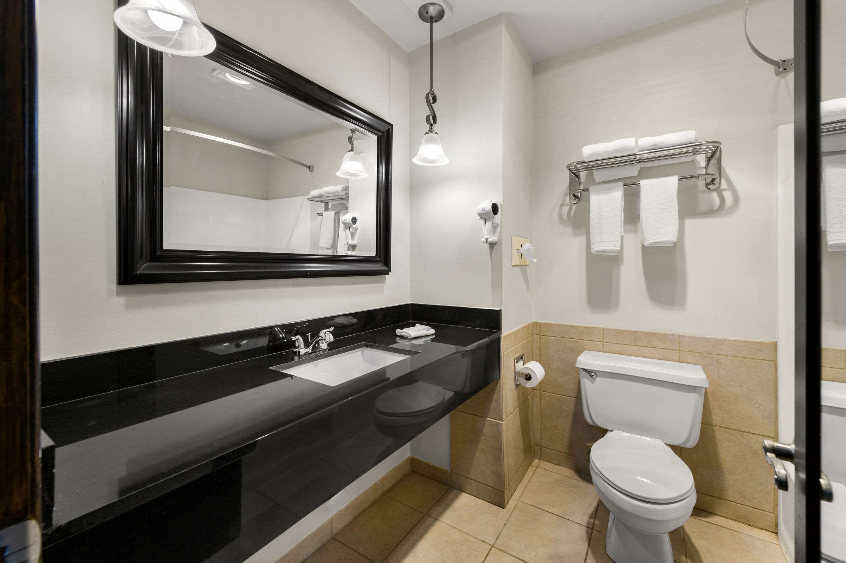 Un baño moderno con lavamanos de superficie negra, un espejo, un inodoro y un perchero para toallas.