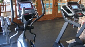 Two exercise bikes with digital displays in a gym with brick walls and windows. - Suburban Studios Kansas City Airport North (Platte City)