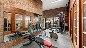 A gym with brick walls, various exercise equipment, and large windows. - Suburban Studios Kansas City Airport North (Platte City)