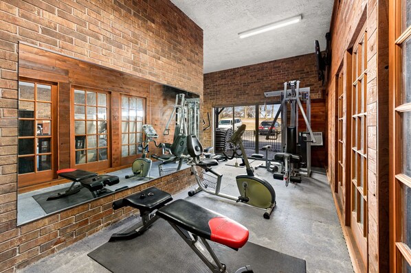 Un gimnasio con paredes de ladrillo, varios equipos de ejercicio y ventanas grandes.