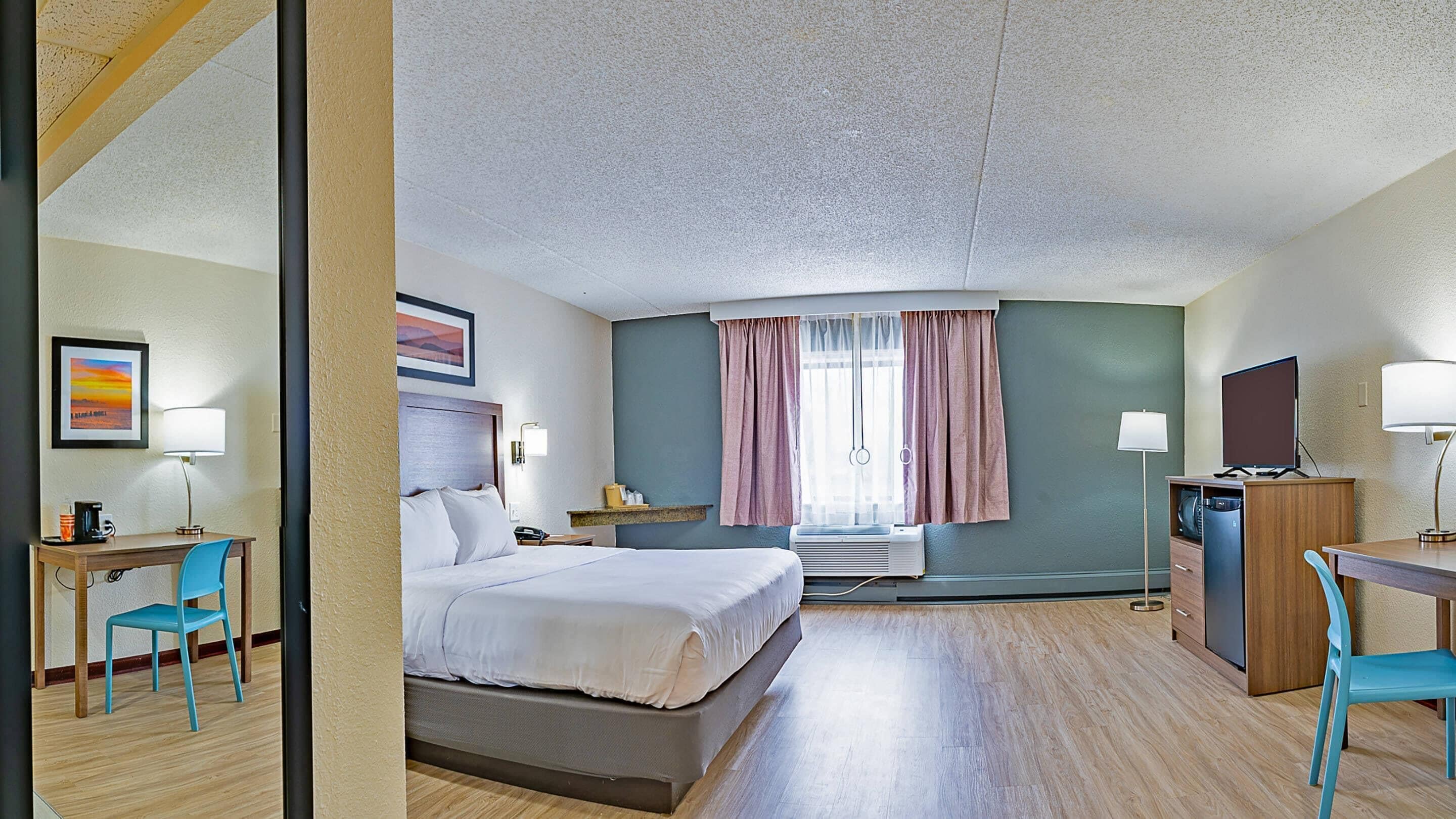 A hotel room with a bed, desk, chair, and a television.