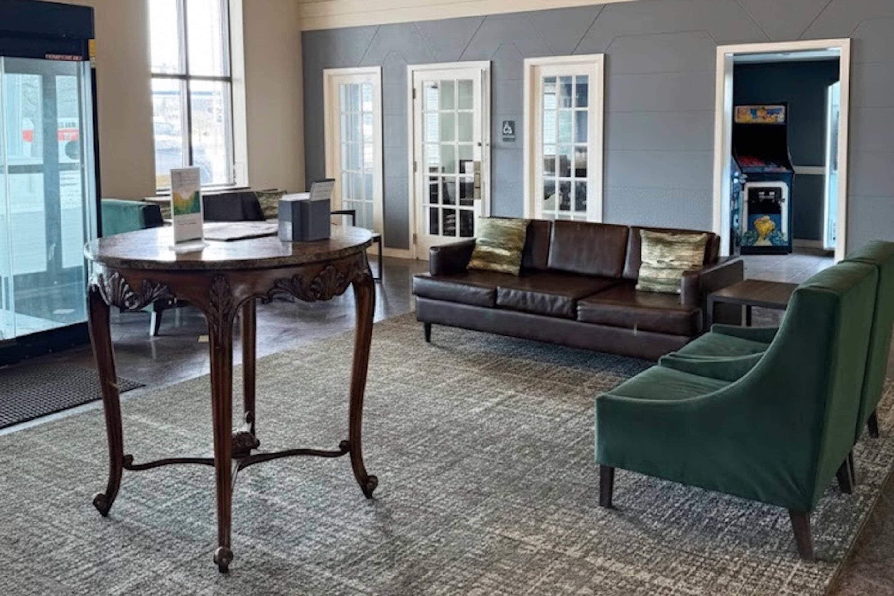 Um hall com um sofá de couro marrom, uma poltrona verde, uma mesa de madeira e uma porta de vidro que dá para o exterior.