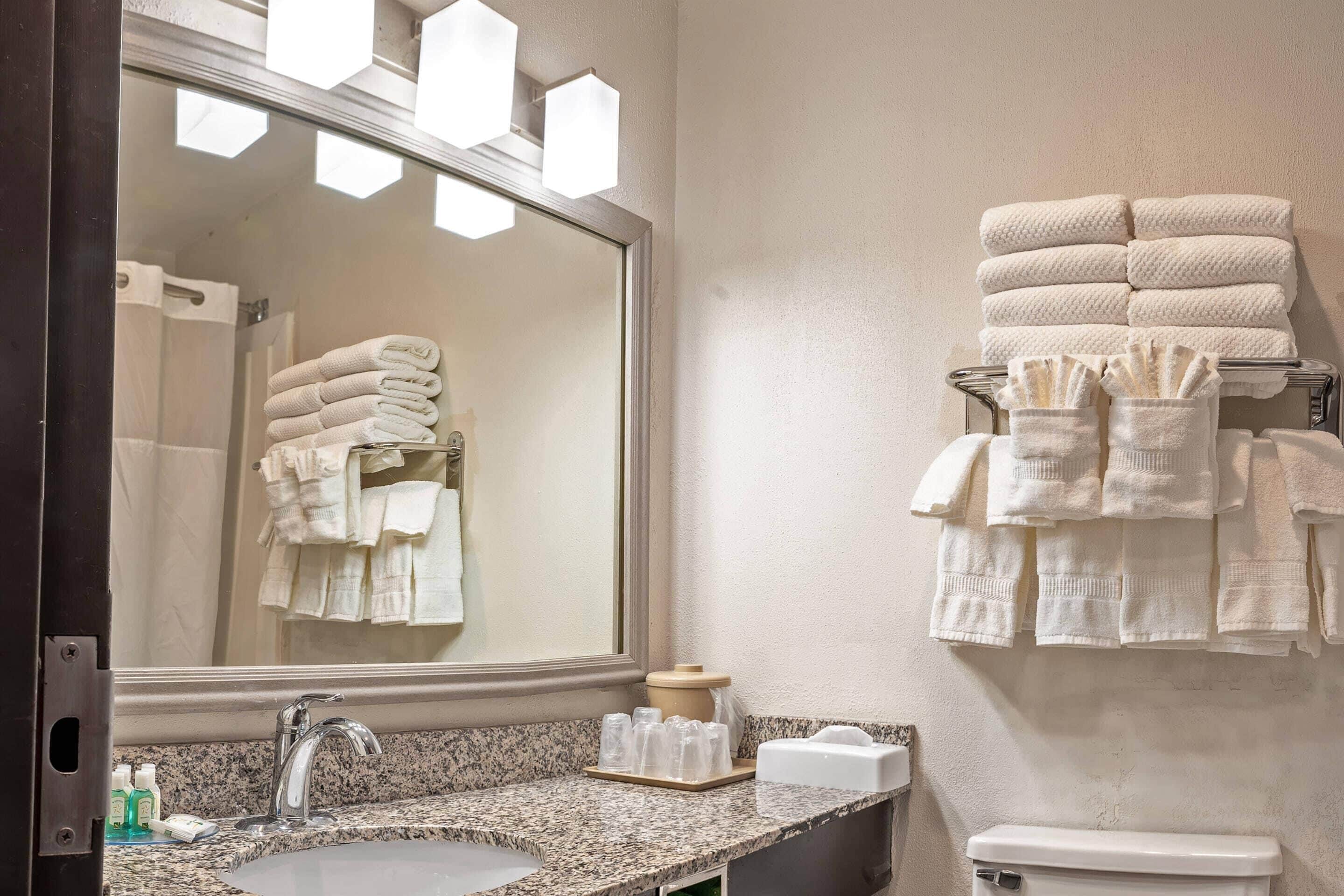 A bathroom with a granite countertop, a sink, a mirror, and a stack of towels on a rack.