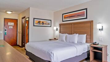 A hotel room with a large bed, wooden headboard, two bedside tables with lamps, and a door with a mirror.