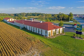 A hotel with a red roof and white walls, situated next to a road and fields.