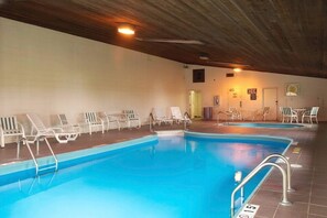 An indoor swimming pool with multiple lanes, surrounded by white lounge chairs and a wooden ceiling.