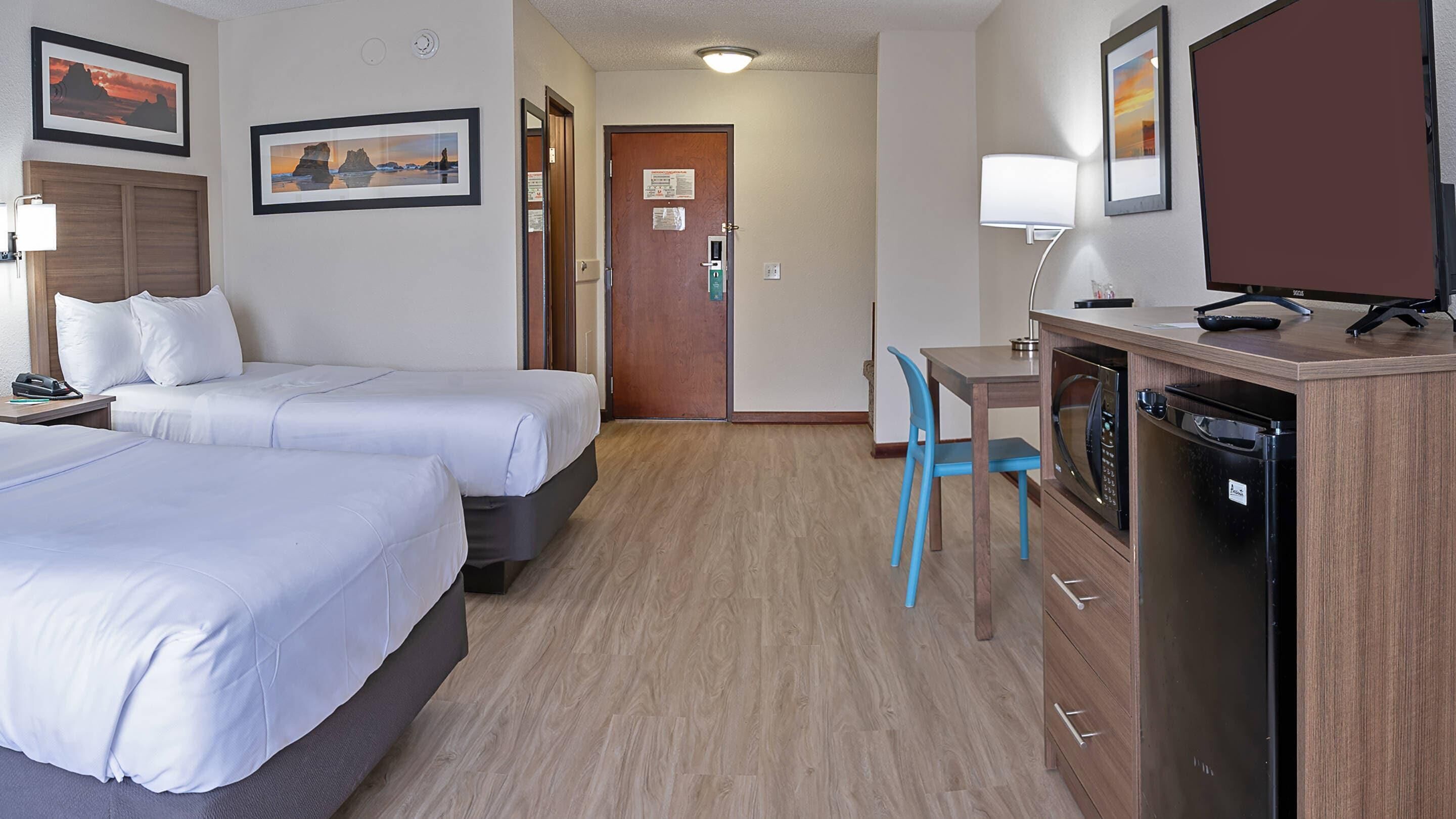 Una habitación de hotel con dos camas, un escritorio con una silla, un microondas y un refrigerador.
