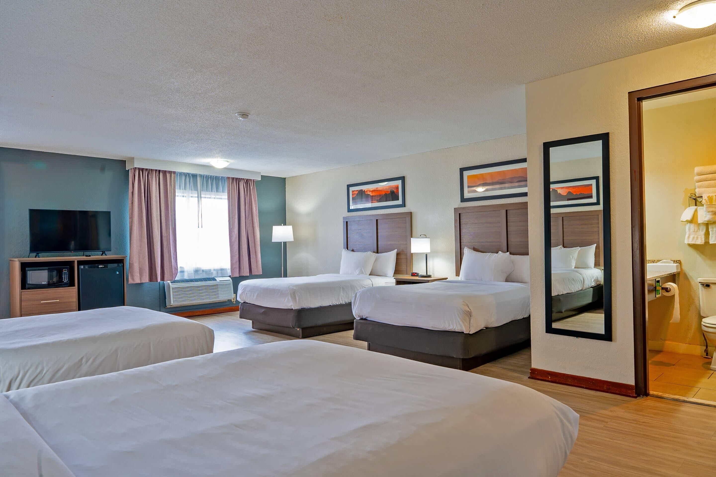 A hotel room with three beds, a television, a desk, and an air conditioning unit.