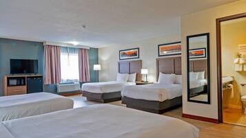 A hotel room with three beds, a television, a desk, and an air conditioning unit.