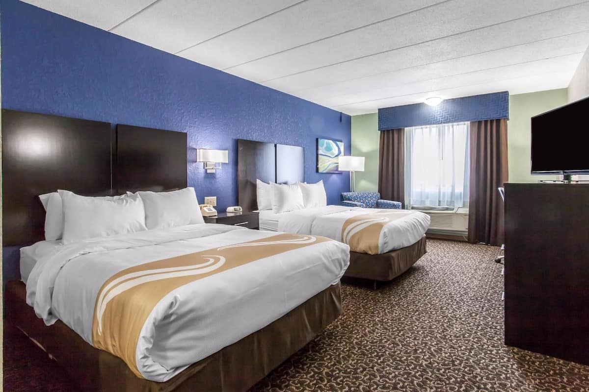 A hotel room with two beds, a television, a desk, and a window with curtains.