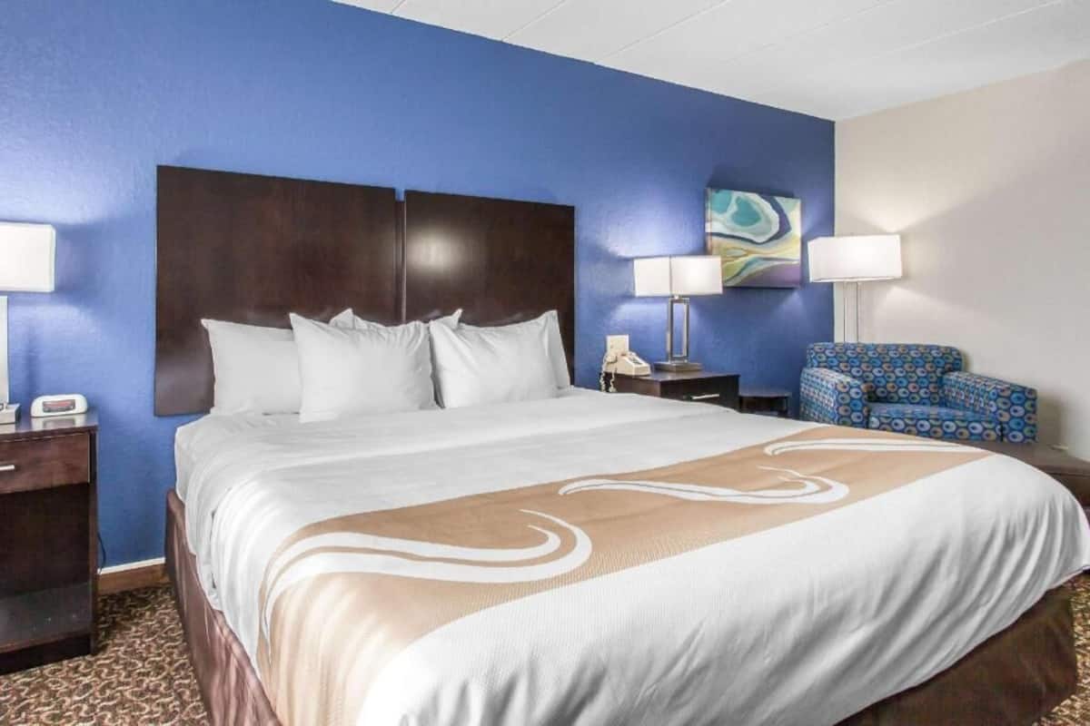A hotel room with a large bed, two bedside tables, a chair, and a painting on the wall.