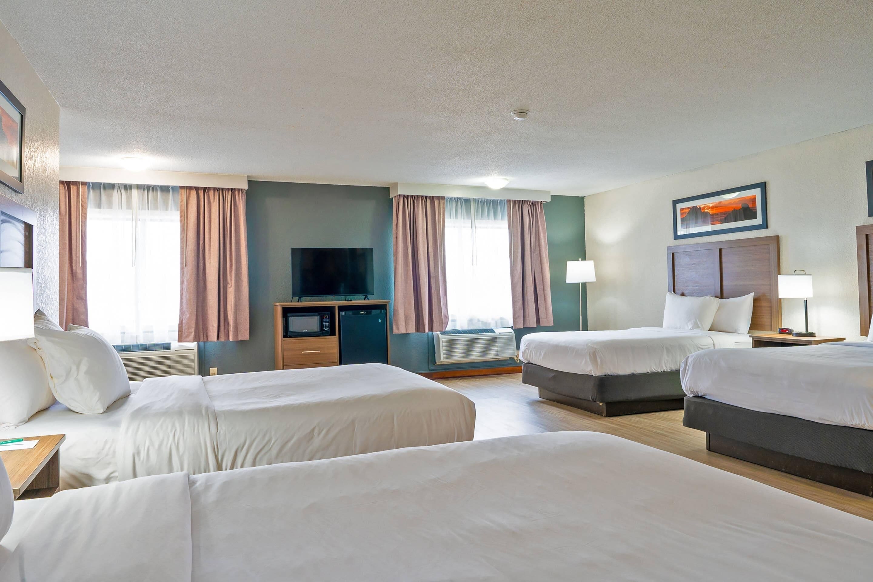A hotel room with two single beds, a TV, a desk, and a window with curtains.