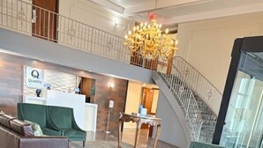 A spacious lobby with a reception desk, a green armchair, a brown leather sofa, and a chandelier. - Quality Inn Milan - Sandusky (Milan)