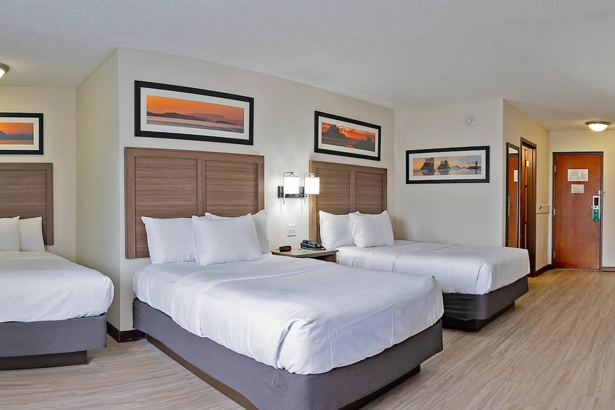 A hotel room with three beds, wooden headboards, and framed pictures on the walls.