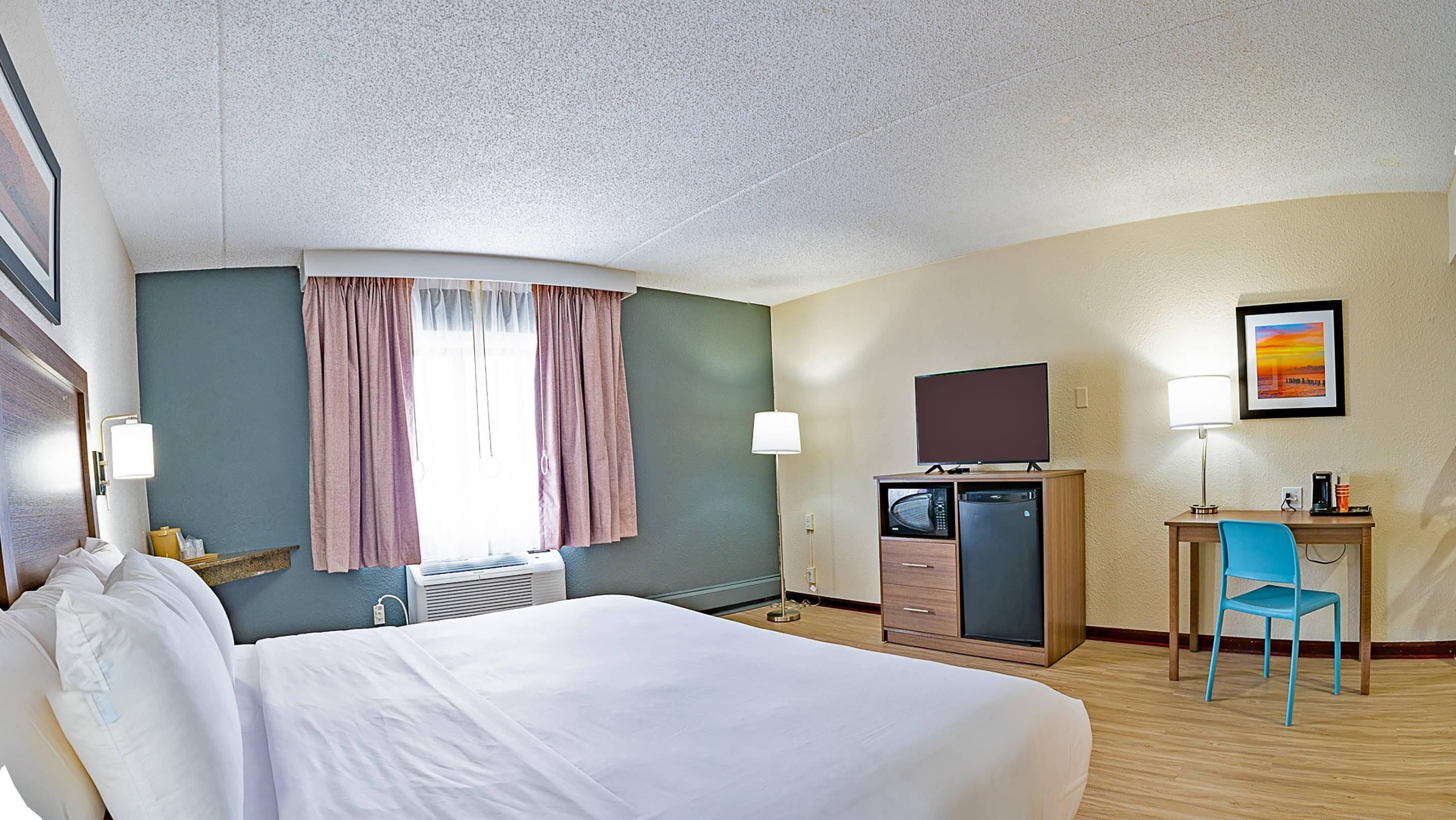 A hotel room with a bed, a desk with a chair, a television, and a microwave.