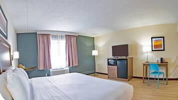 A hotel room with a bed, a desk with a chair, a television, and a microwave.