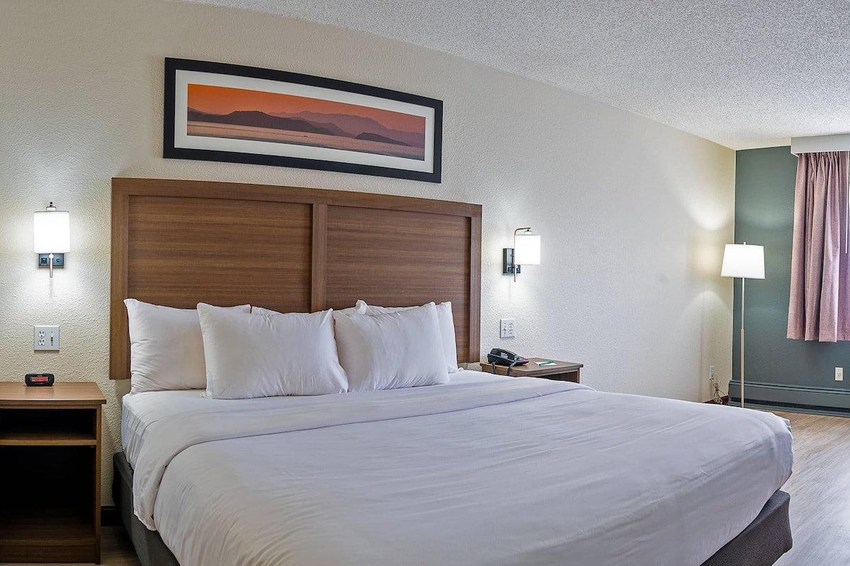 A neatly made bed with white linens, a wooden headboard, and two bedside lamps.