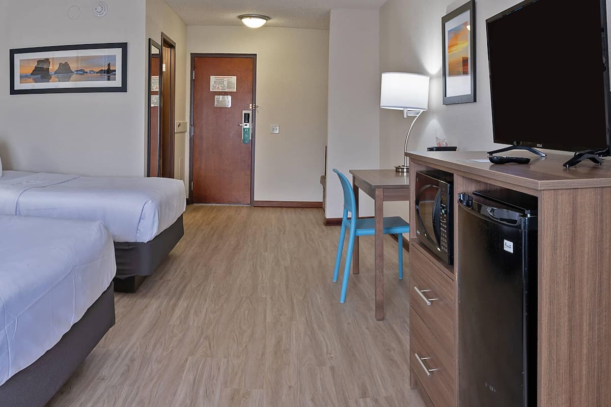 A hotel room with two beds, a desk with a chair, a microwave, and a TV.