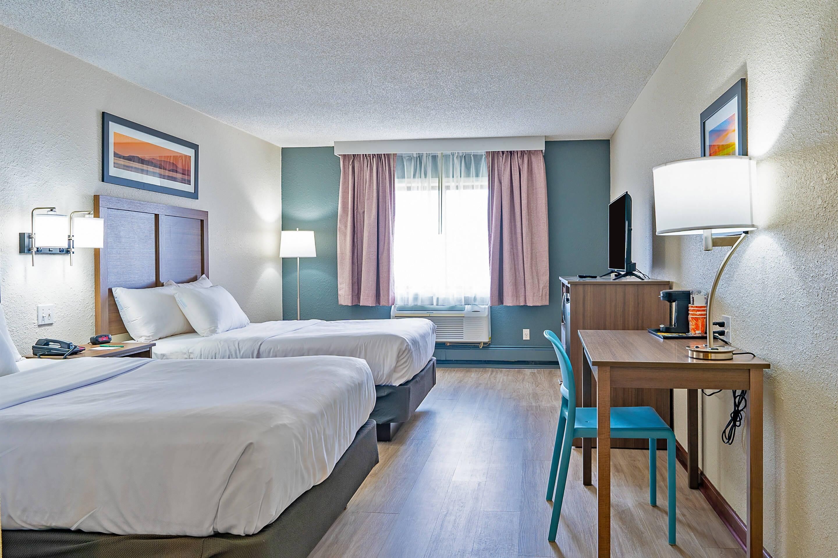 A hotel room with two beds, a desk, a chair, a TV, and a window with curtains.