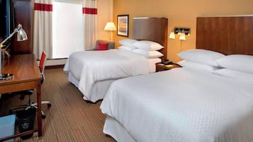 A hotel room with two beds, a desk, a chair, a TV, and a lamp.