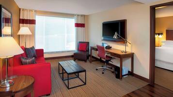 Una habitación de hotel con sofá rojo, una pequeña mesa de madera, un escritorio con silla, un televisor montado en la pared y una cama.