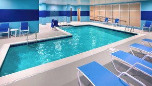 Una piscina interior con paredes de azulejos azules y blancos, agua cristalina y varias sillas reclinables azules alrededor de la zona de la piscina.