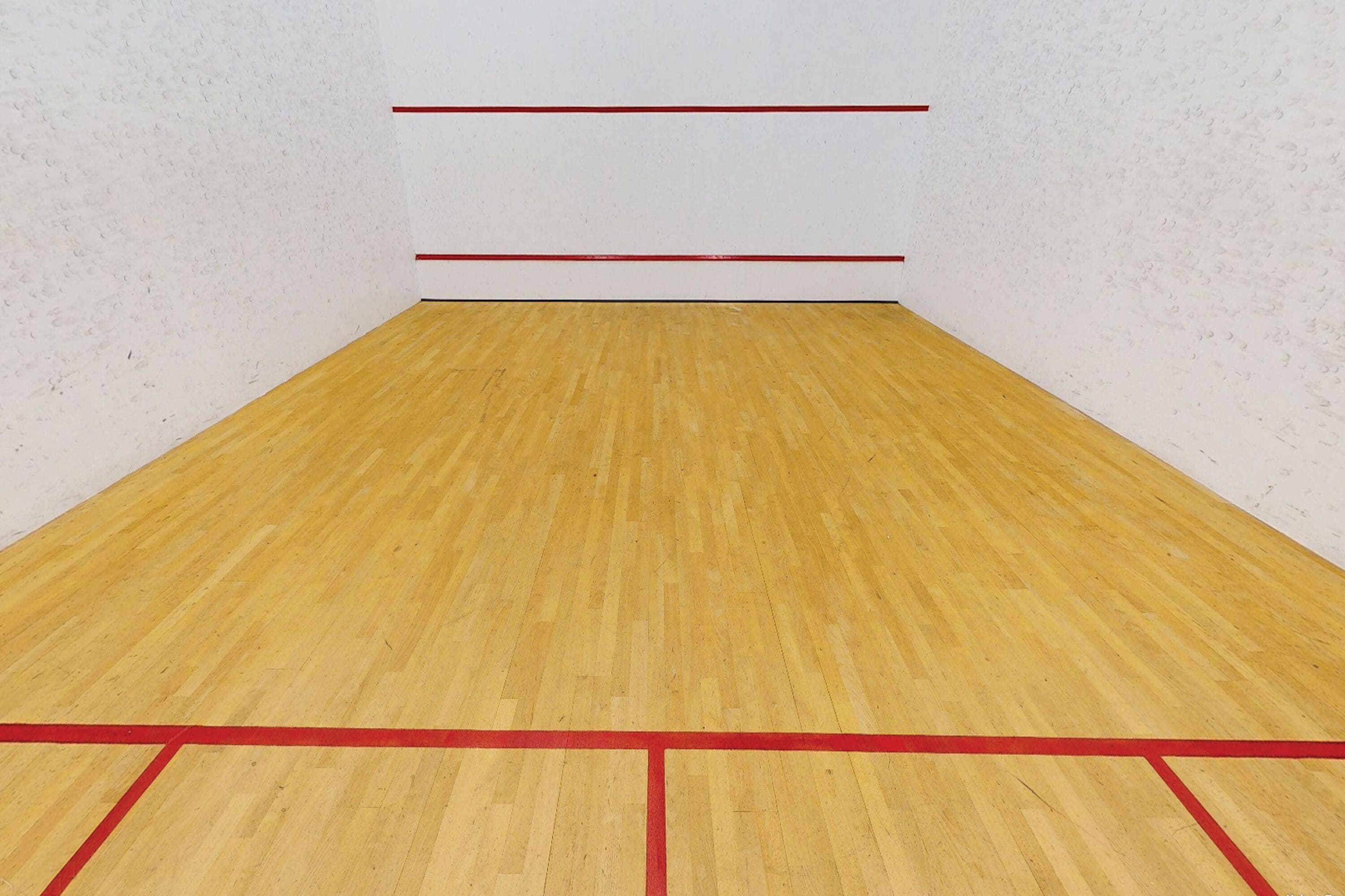 A squash court with wooden flooring and red boundary lines.