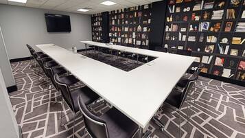 Un salón de conferencias con una larga mesa, sillas y una estantería llena de libros y objetos decorativos.