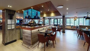 A modern bar area with a wooden ceiling, a large flat-screen TV, and a bar counter with stools. - Village Hotel Warrington (Warrington)