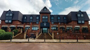 A brick building with multiple storefronts including a pub, grill, Starbucks, and a works shop. - Village Hotel Warrington (Warrington)