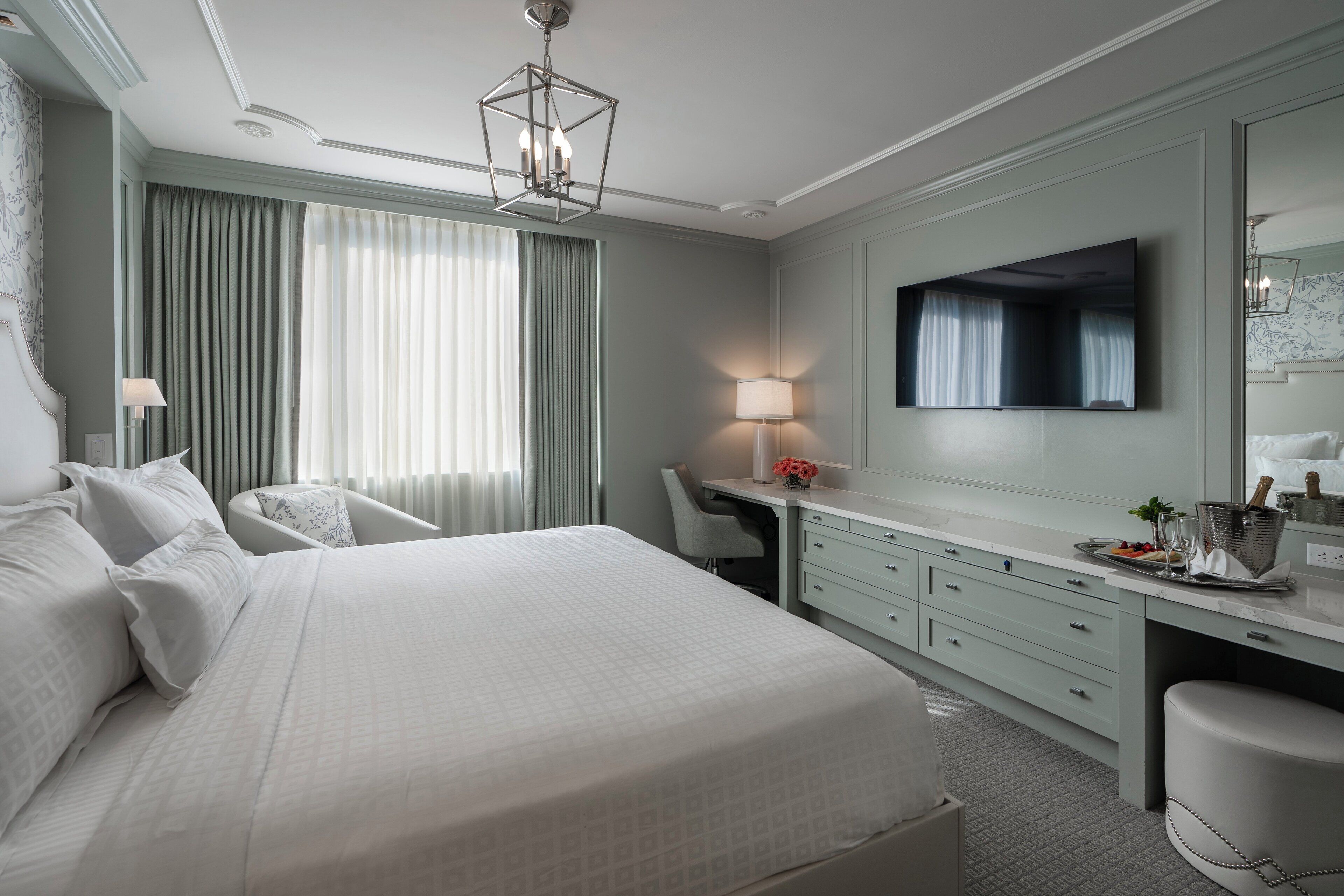 A hotel room with a large bed, a desk, a chair, a TV, and a mirror.