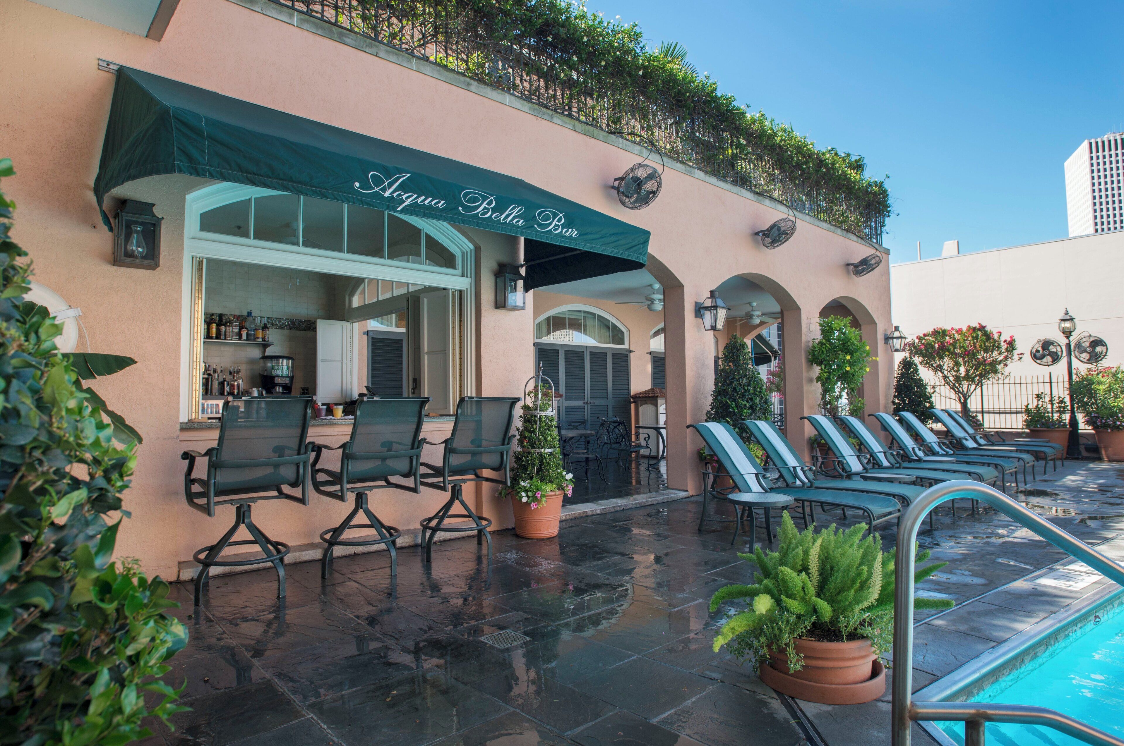 A poolside area with lounge chairs and a bar named "Acqua Bella Bar" with a green awning.