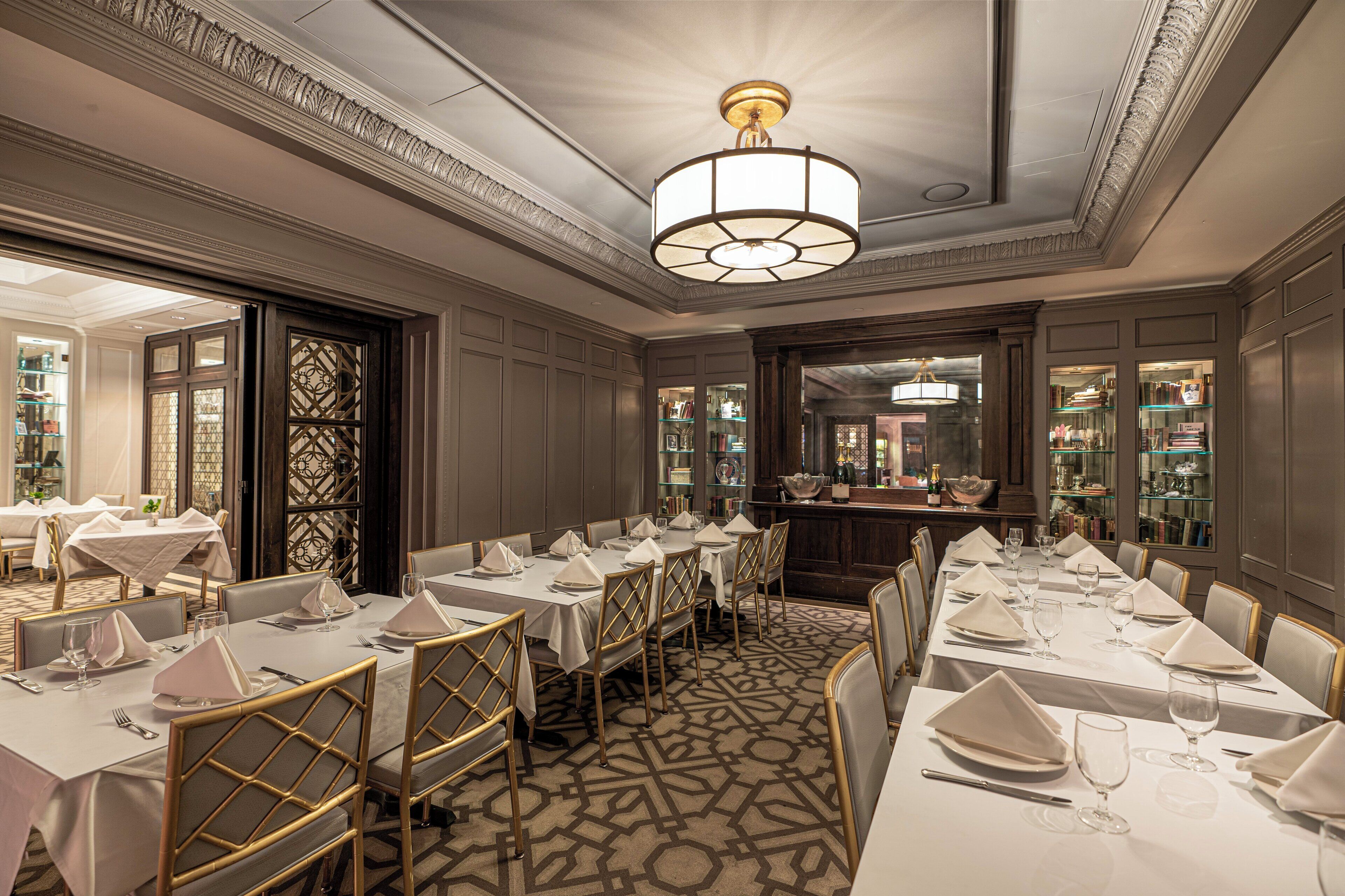 Uma sala de jantar formal com mesas longas, cadeiras douradas e um candelabro.