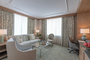A hotel room with a sofa, armchairs, a coffee table, and a desk with a lamp.