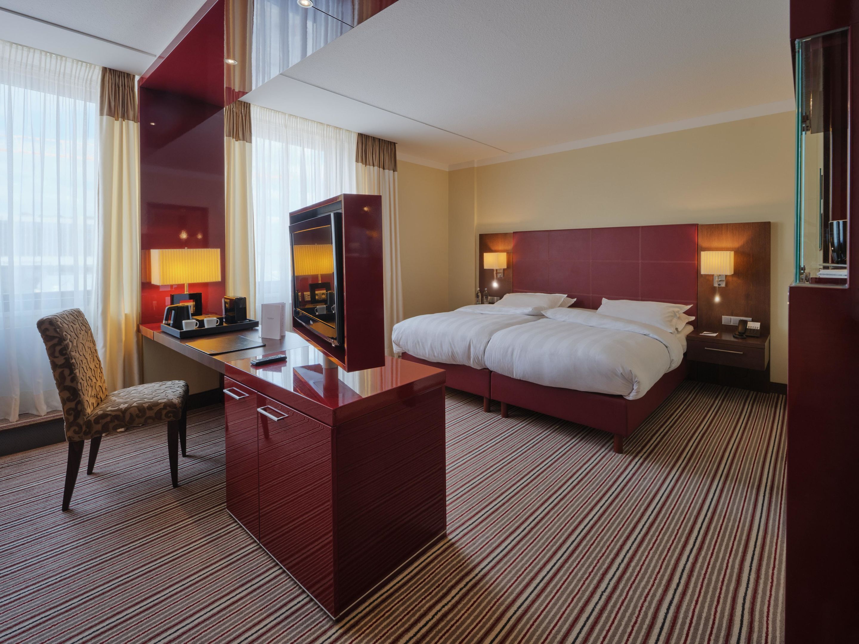 A hotel room with a large bed, a desk with a chair, a TV, and a minibar.