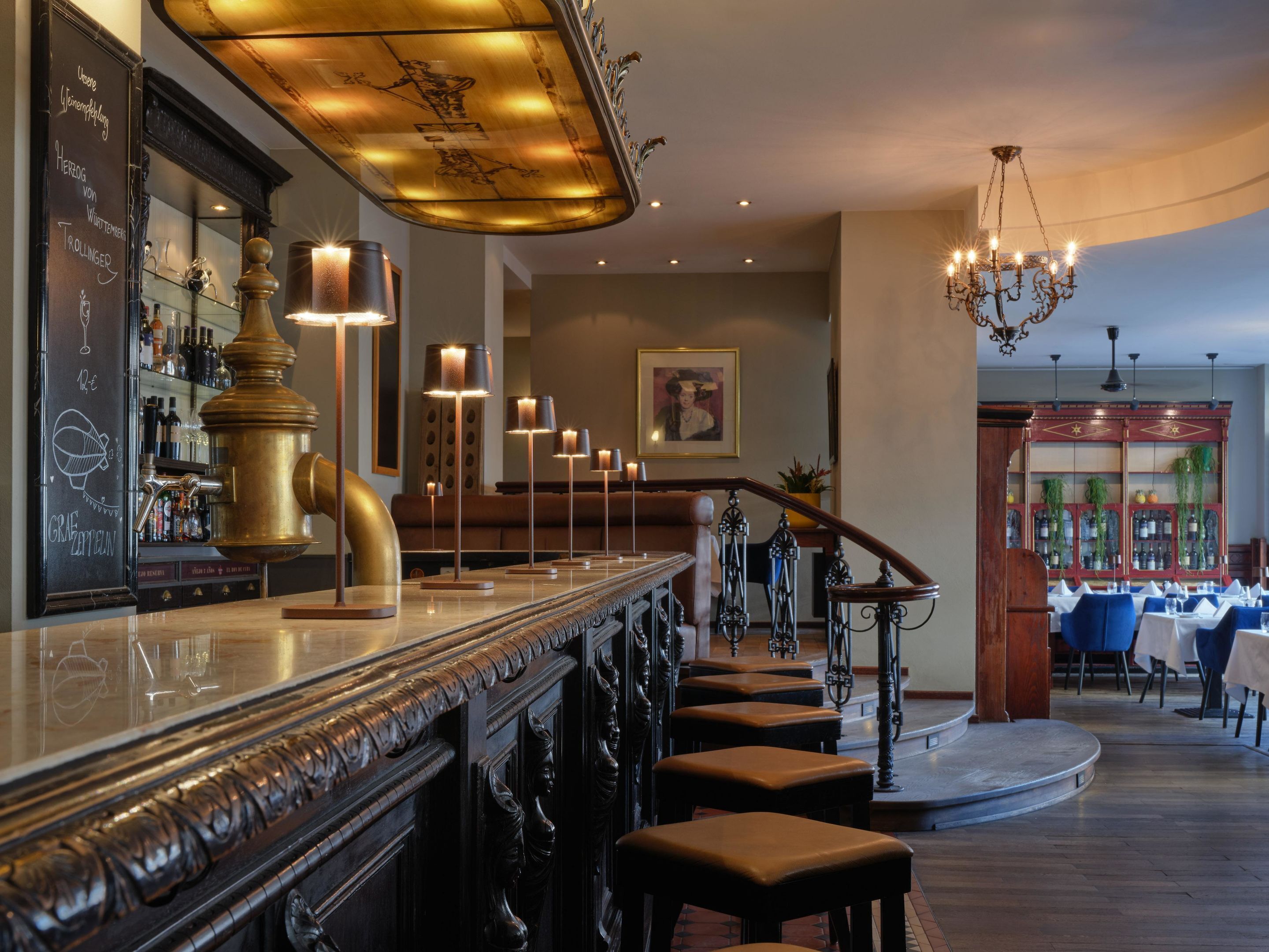 A bar area with a polished counter, stools, and a staircase leading to a dining area.