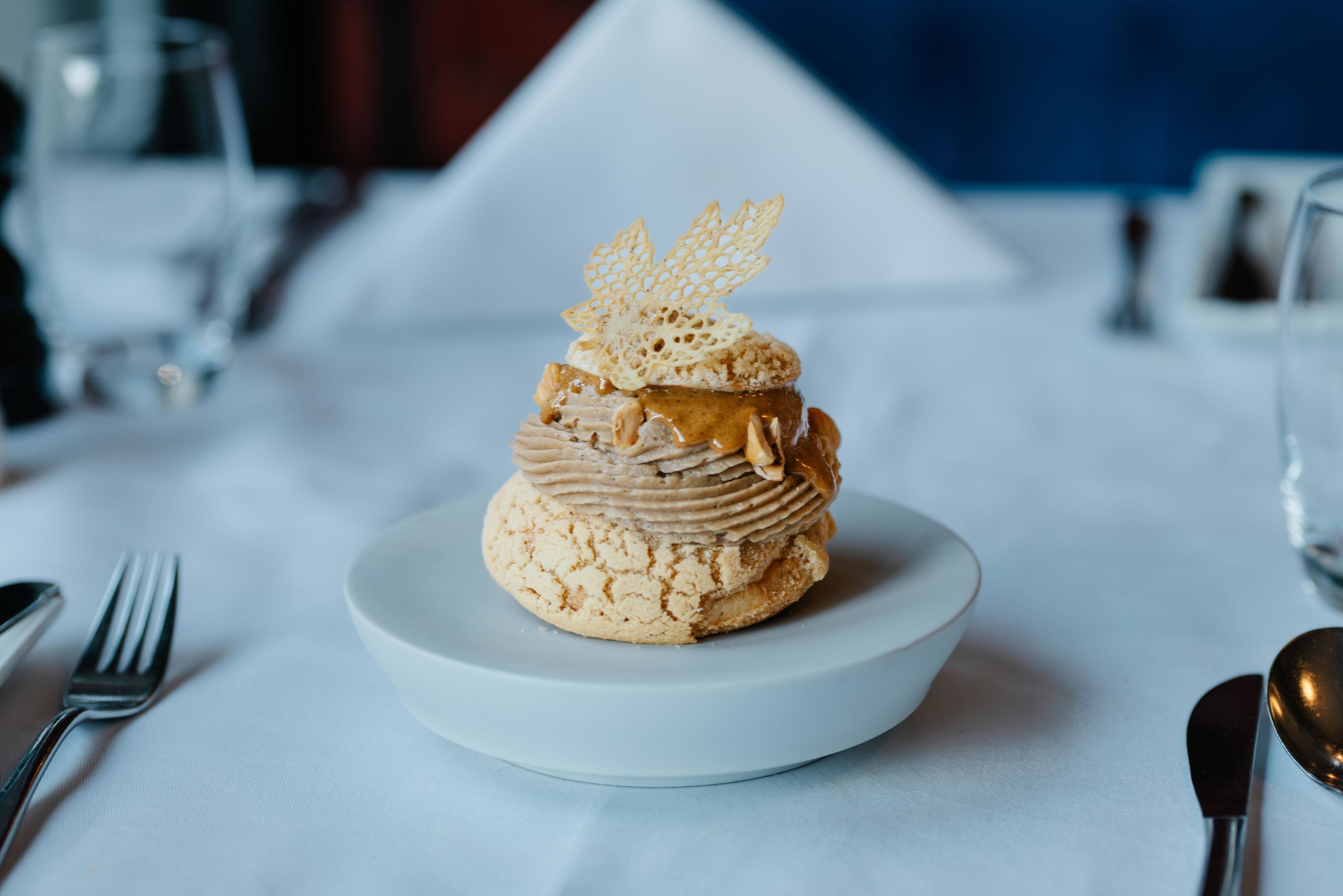 A dessert on a white plate with a decorative leaf on top, placed on a table with a white tablecloth.