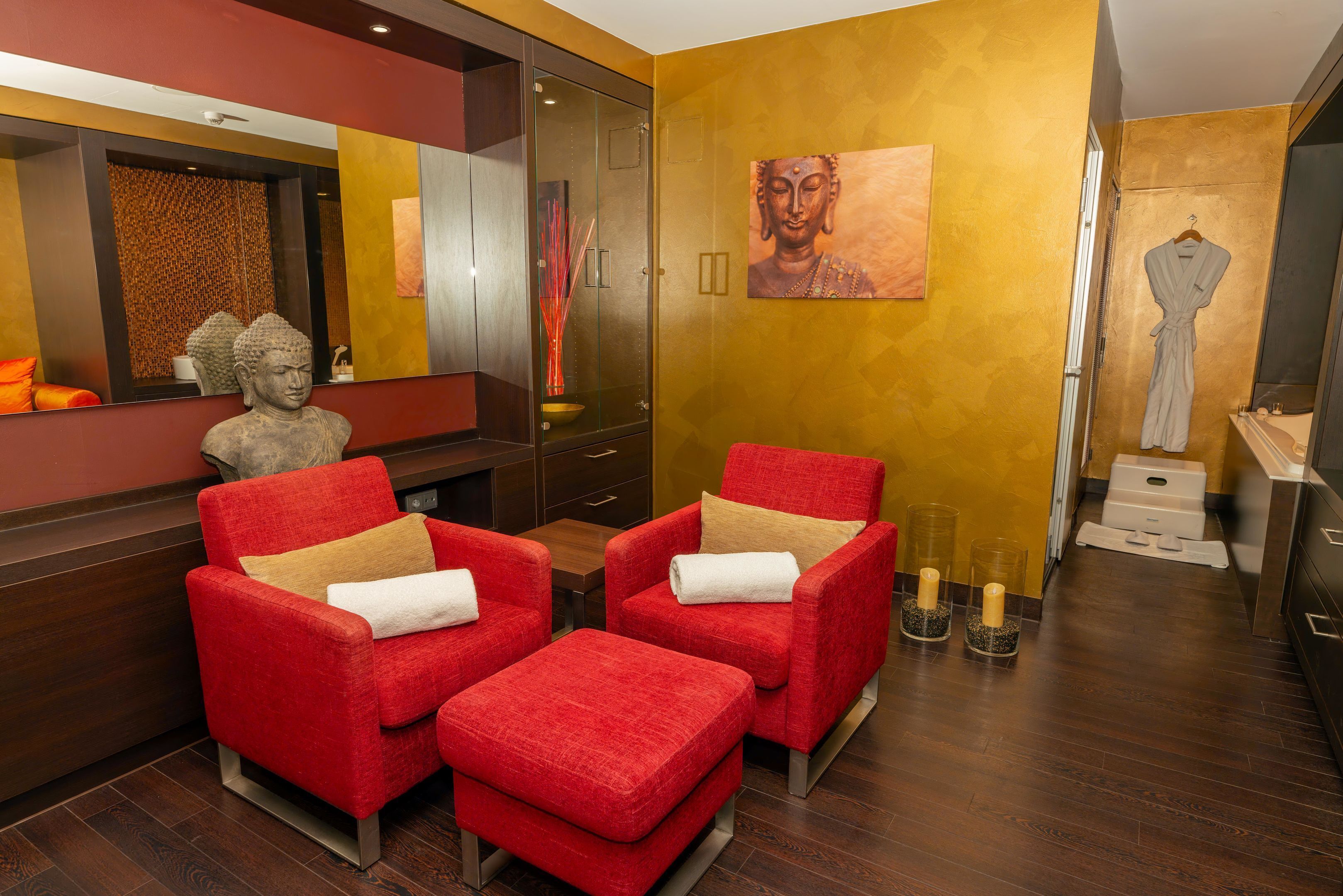 A modern room with two red armchairs, a small table, a Buddha statue, and a painting on the wall.