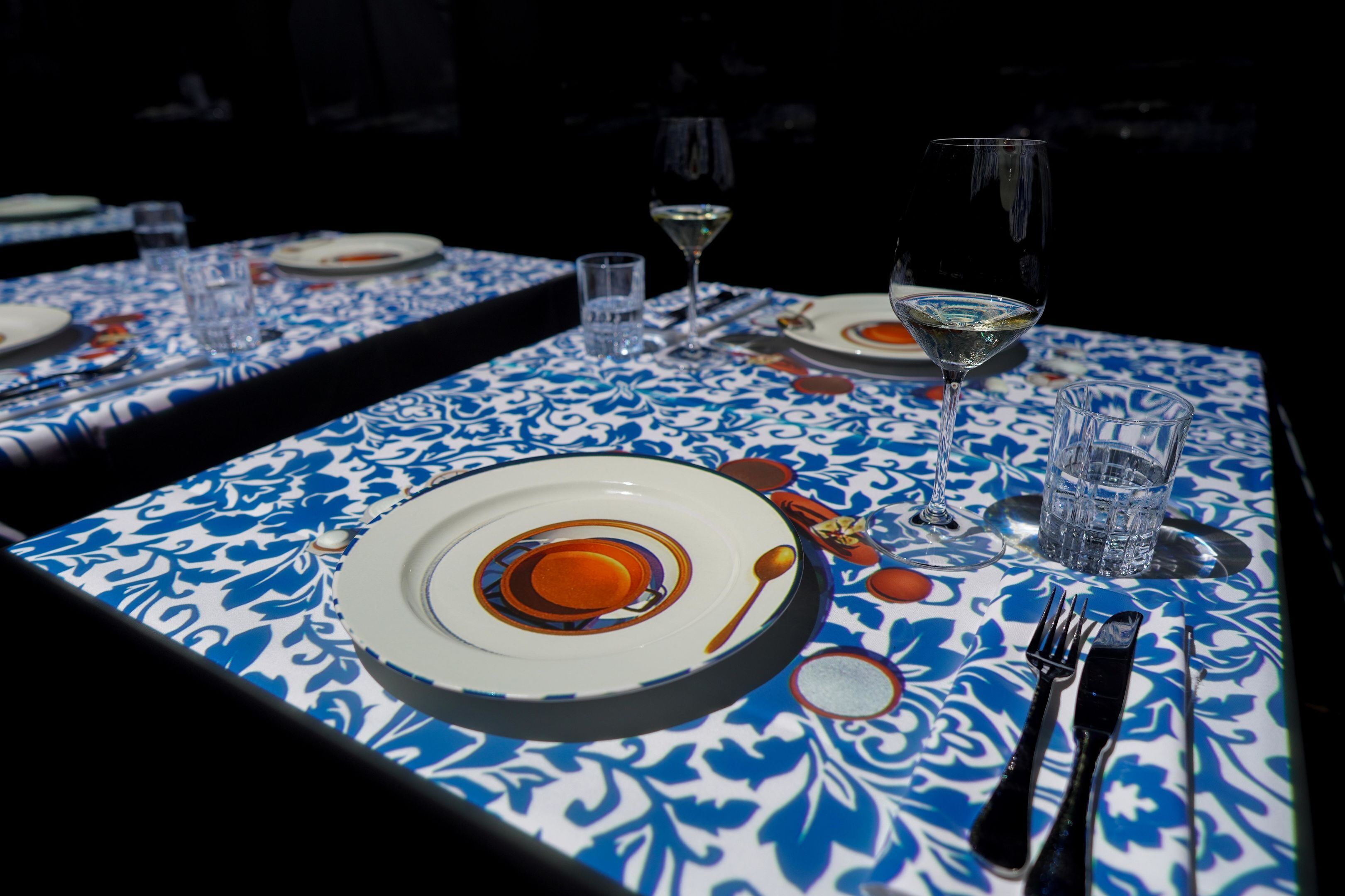 Una mesa de comedor con platos, cubiertos, vasos y una copa de vino.