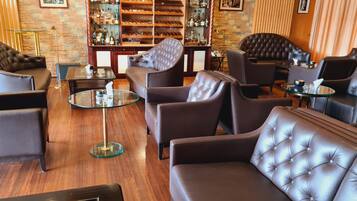 A modern lounge area with leather sofas, a glass coffee table, and a bar stocked with liquor bottles.