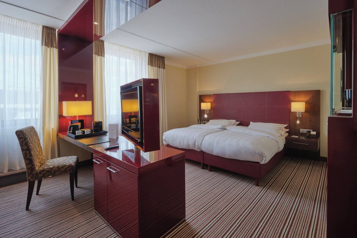 Habitación de hotel con una cama grande, un escritorio con silla, televisor y minibar.