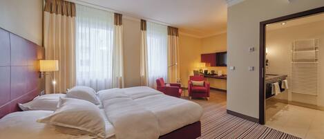 A hotel room with a large bed, a desk, a chair, and a bathroom visible through an open door.