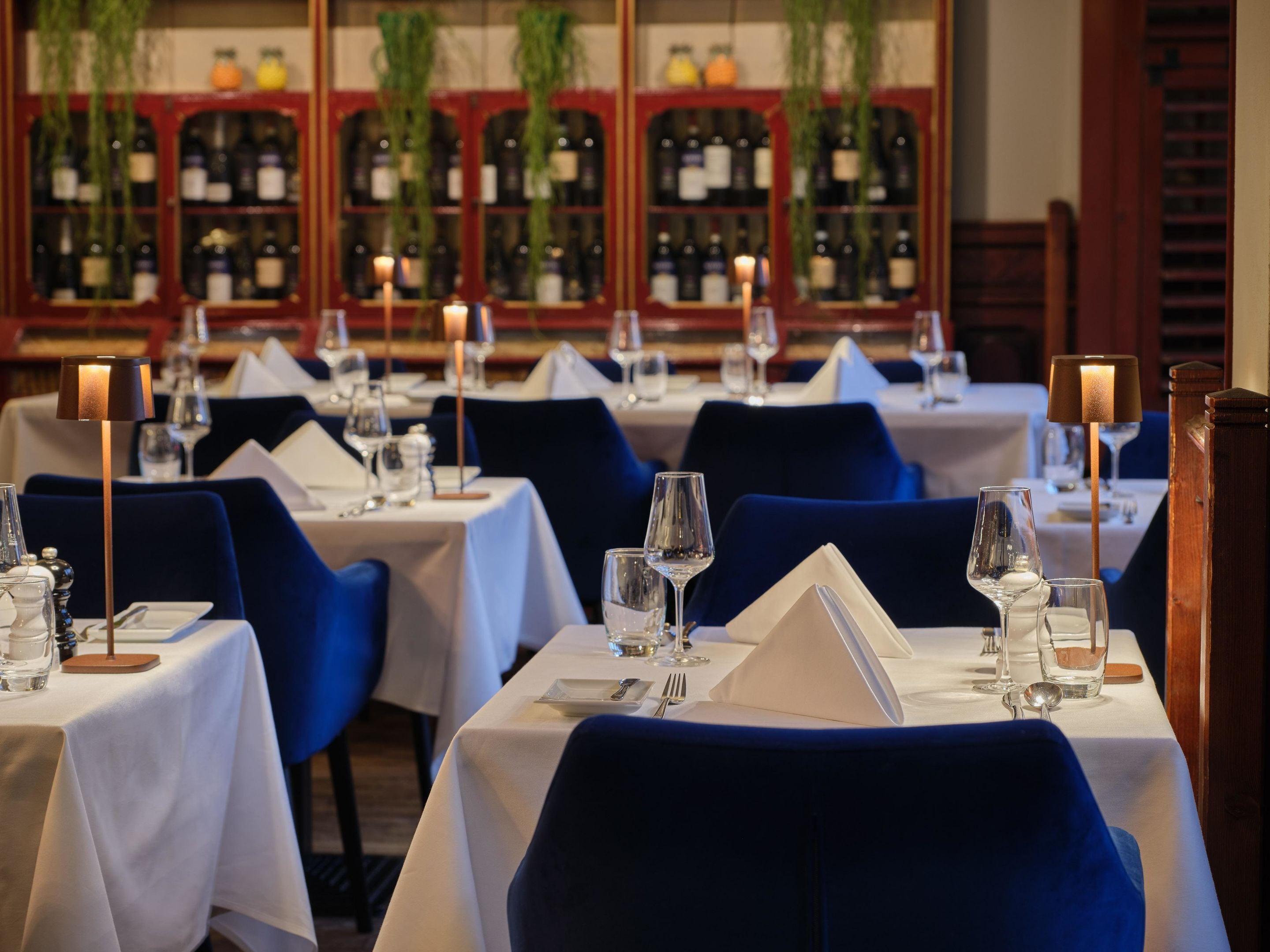 Un restaurant où les tables sont dressées pour le service, avec des chaises bleues et des nappes blanches.