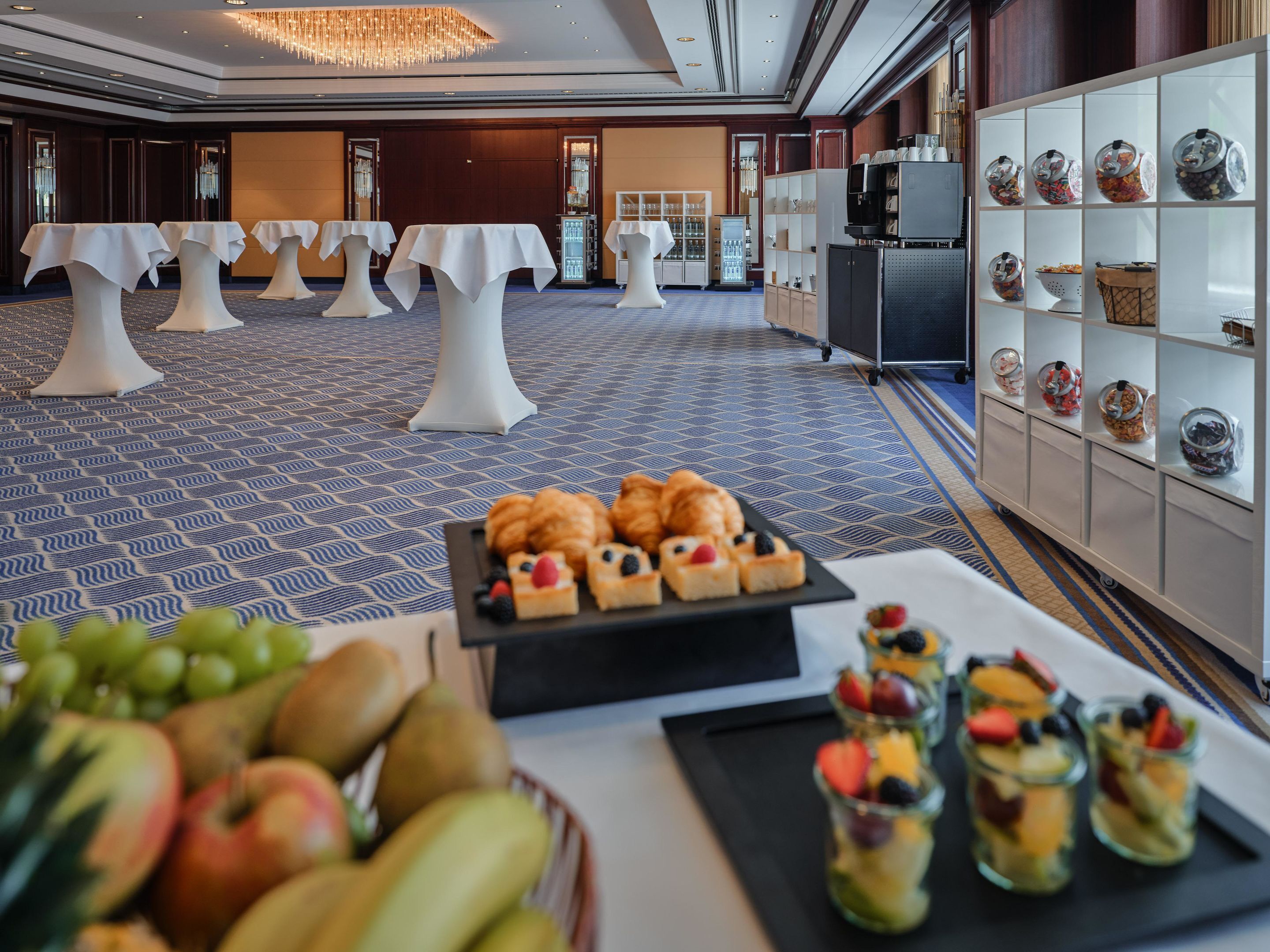 Un hall d’hôtel avec des tables, un présentoir de fruits et un espace dédié aux boissons.