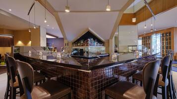 Uma área de bar moderna com uma ilha grande, banquetas e uma variedade de garrafas e copos.