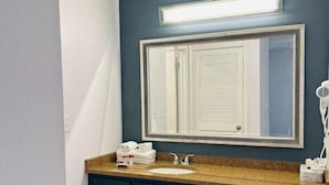 A bathroom with a dark blue wall, a white sink, and a large mirror with a decorative frame. - Extended Stay of Charleston (North Charleston)