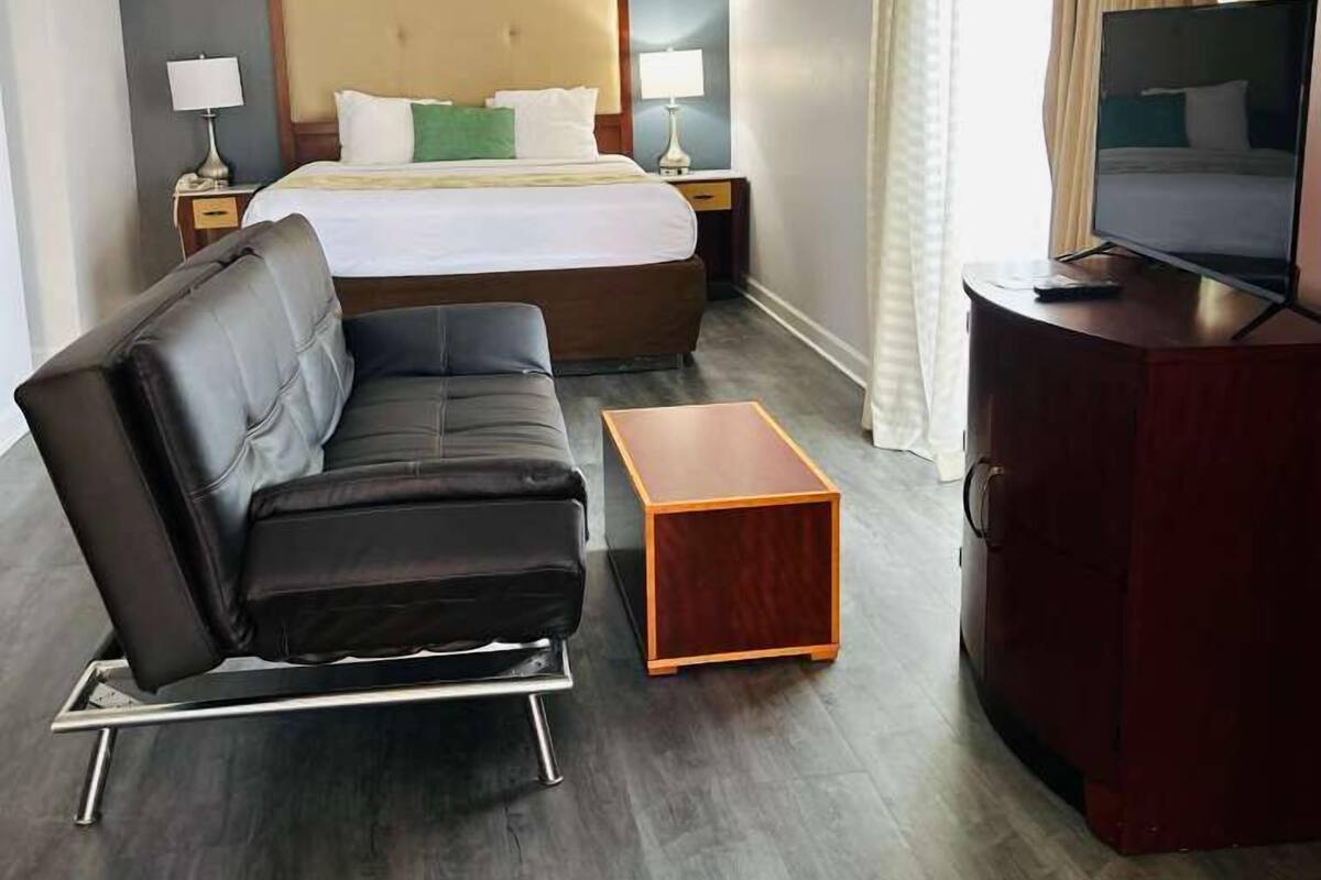 A hotel room with a bed, a sofa, a TV, a small wooden table, and a cabinet.