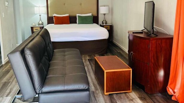 A hotel room with a large bed, a leather sofa, a wooden side table, and a TV. - Extended Stay of Charleston (North Charleston)